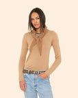 Woman wearing a beige sweater with a scarf and blue jeans on a beige background