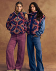 Two women wearing patterned outfits against a brown background