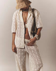 Person wearing a white lace outfit with a straw hat against a plain background