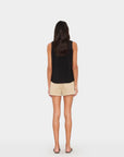 Woman wearing a black sleeveless top and beige shorts on a white background