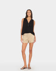 Woman wearing a black sleeveless top and beige shorts on a white background