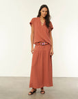 Woman wearing a rust-colored outfit with a belt against a white background