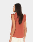 Woman wearing a rust-colored sleeveless top with ruffled shoulders on a white background