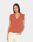 Woman wearing a rust-colored sleeveless top with ruffled shoulders on a light gray background
