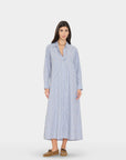 A woman modeling a long-sleeve, button-front midi dress with vertical blue, white, and light orange stripes, paired with brown shoes, against a light gray studio background.