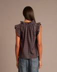 Woman wearing a patterned top and jeans against a brown background