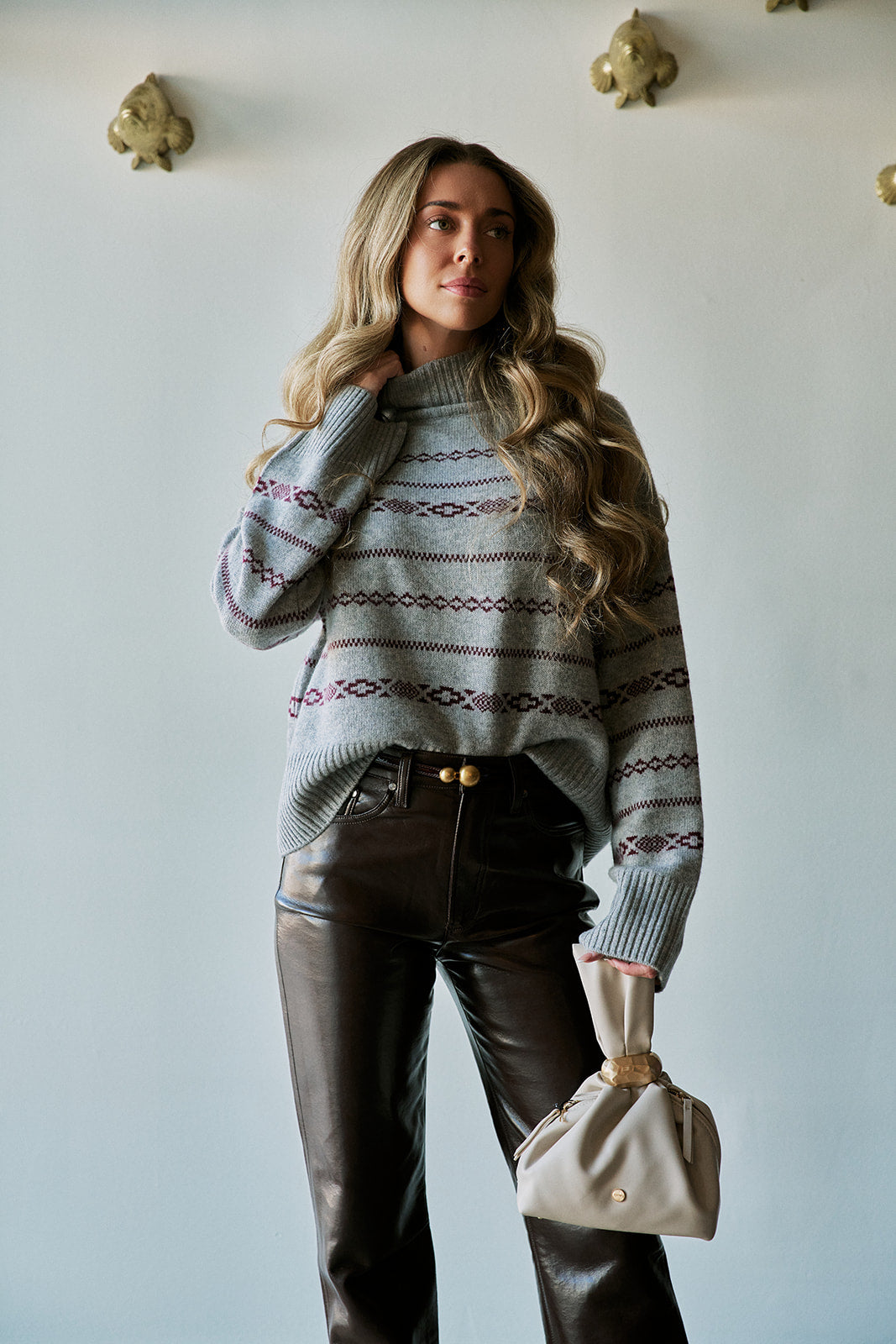model wearing a grey fairisle sweater with coated jeans, a belt with two gold balls, holding an ivory bag 