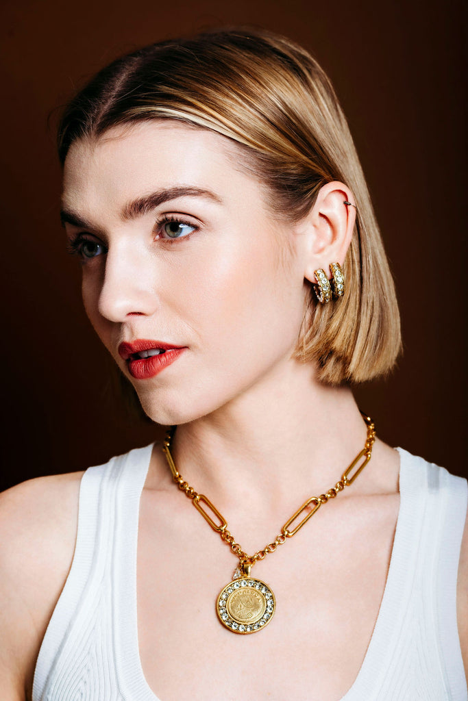 Woman wearing a gold necklace and earrings against a brown background