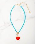 Turquoise beaded necklace with a red heart pendant on a white background