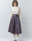 Person wearing a beige sweater, dark purple leather skirt, and white shoes on a plain background