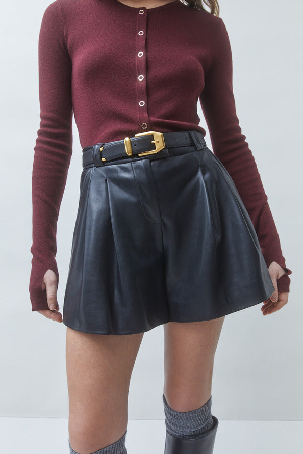 A model wearing a burgundy long-sleeve button-up knit top and a black faux-leather pleated mini skirt with a black belt and gold buckle.