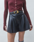 A model wearing a burgundy long-sleeve button-up knit top and a black faux-leather pleated mini skirt with a black belt and gold buckle.