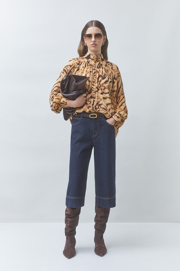Woman wearing a leopard print blouse, dark jeans, and brown knee-high boots on a white background