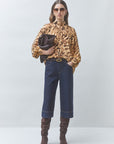 Woman wearing a leopard print blouse, dark jeans, and brown knee-high boots on a white background