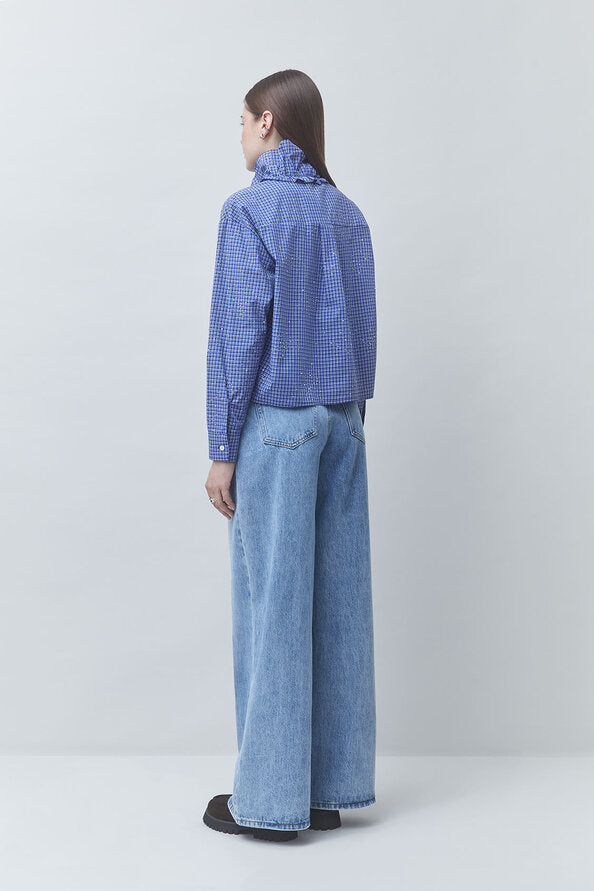A model shown from the back wearing a blue and white checkered long-sleeve shirt and wide-leg light blue jeans, standing against a light gray studio background.
