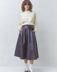 Person wearing a beige sweater, dark purple leather skirt, and white shoes on a plain background