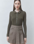 A woman modeling a ribbed long-sleeve polo-knit top in olive green paired with a brown plaid pleated mini skirt, shot against a light gray studio background.