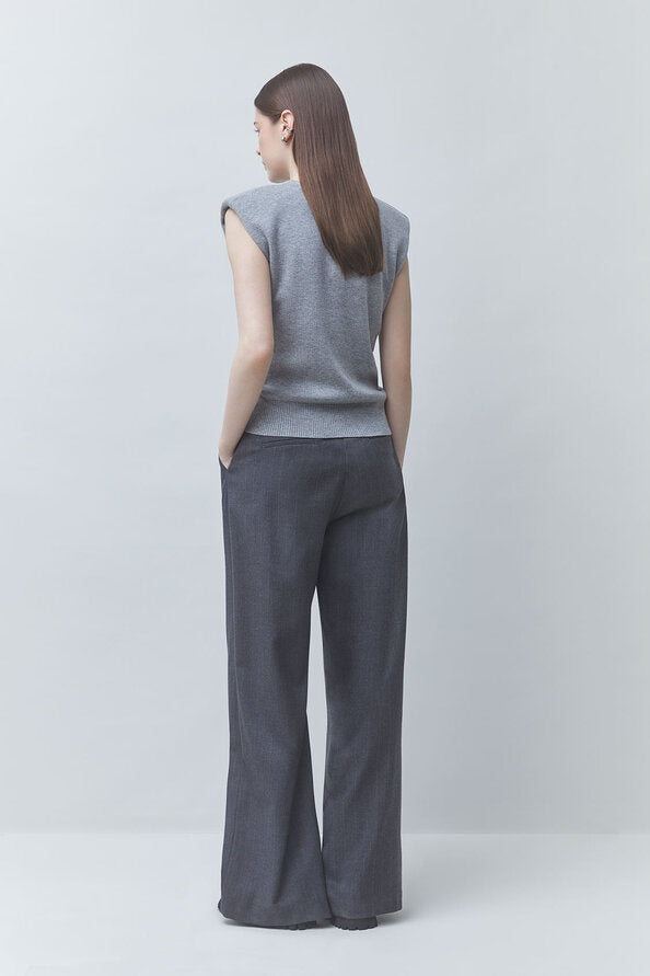 A woman shown from the back wearing a gray sleeveless knit top and dark charcoal wide-leg trousers, standing against a light gray studio background.