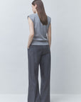 A woman shown from the back wearing a gray sleeveless knit top and dark charcoal wide-leg trousers, standing against a light gray studio background.