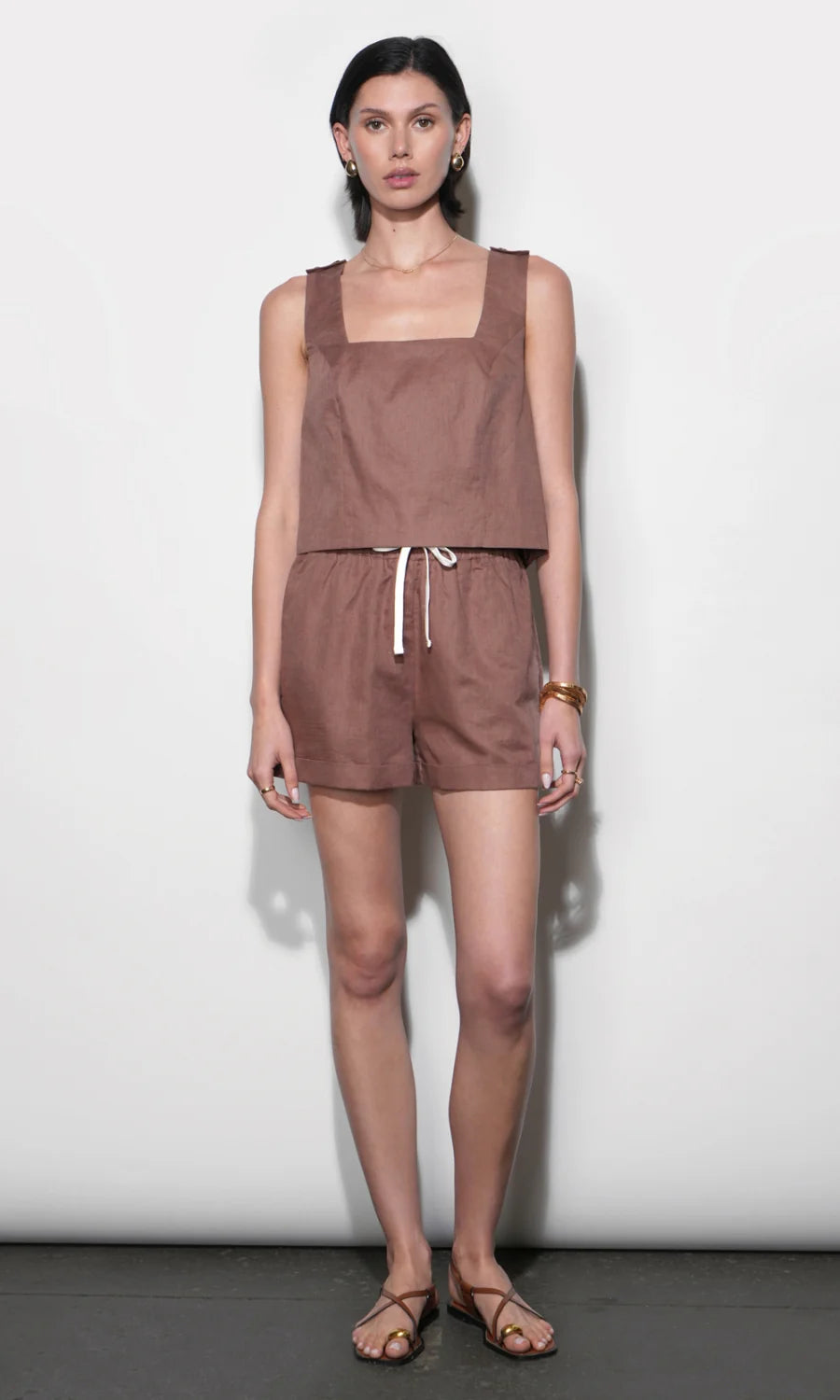 Woman wearing a brown sleeveless top and shorts set against a white background