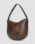 A brown leather crescent-shaped shoulder bag with a black adjustable strap and a subtle embossed logo on the front, set against a light gray background.