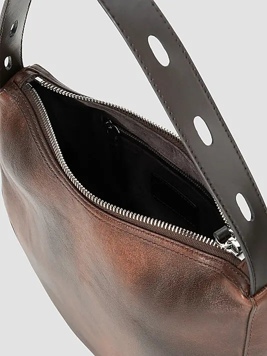 Close-up of a brown leather shoulder bag with an open top zipper, showing a black interior lining and a dark brown strap with oval cutouts against a light gray background.