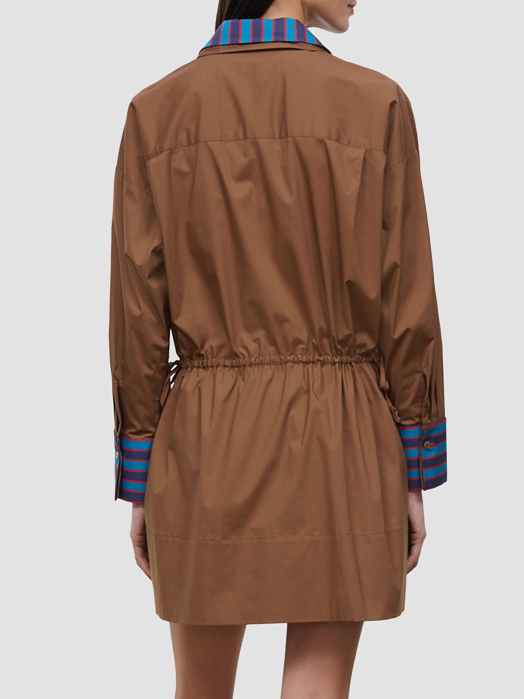 A model shown from the back wearing a brown mini jacket with a striped blue and red collar and cuffs, set against a plain light gray background.