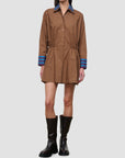 A model wears a brown long-sleeve shirt dress with a blue striped collar and cuffs, paired with black boots, against a solid gray background.