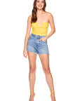 Woman wearing a yellow strapless top and denim shorts on a white background