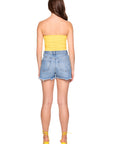 Woman wearing a yellow strapless top and denim shorts on a white background