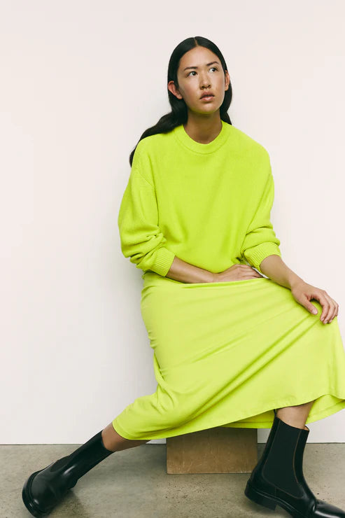Person wearing a bright green outfit sitting against a plain background