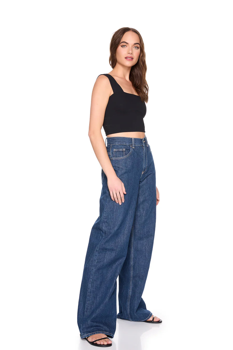 Woman wearing blue jeans and a black top on a white background, side
