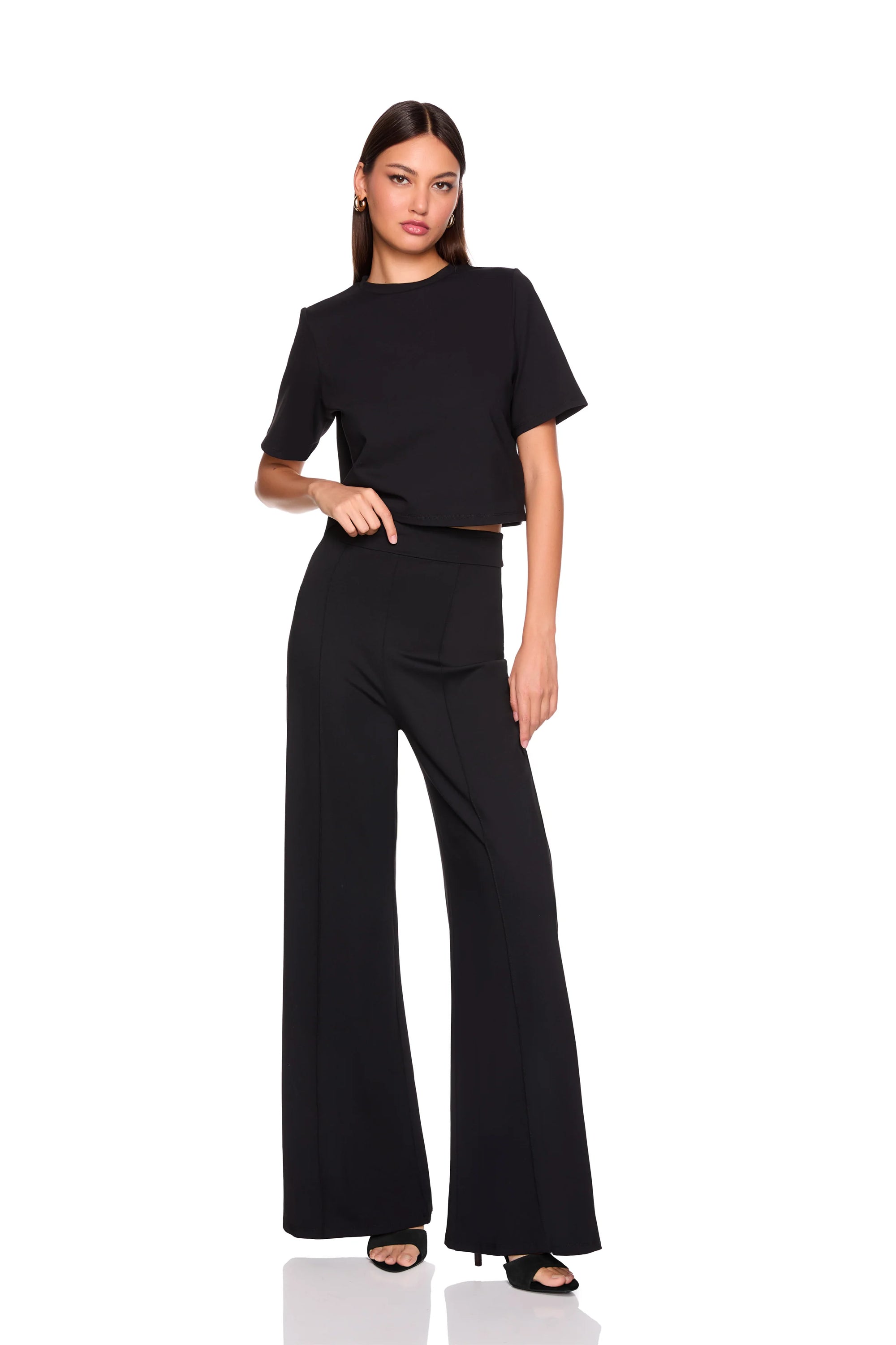 A woman modeling a black short-sleeve mock-neck top and matching high-waisted black wide-leg pants against a plain white background.