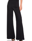 A model wearing black wide-leg high-waisted pants with a front welt pocket, paired with black heeled sandals, shown from the waist down on a white background.