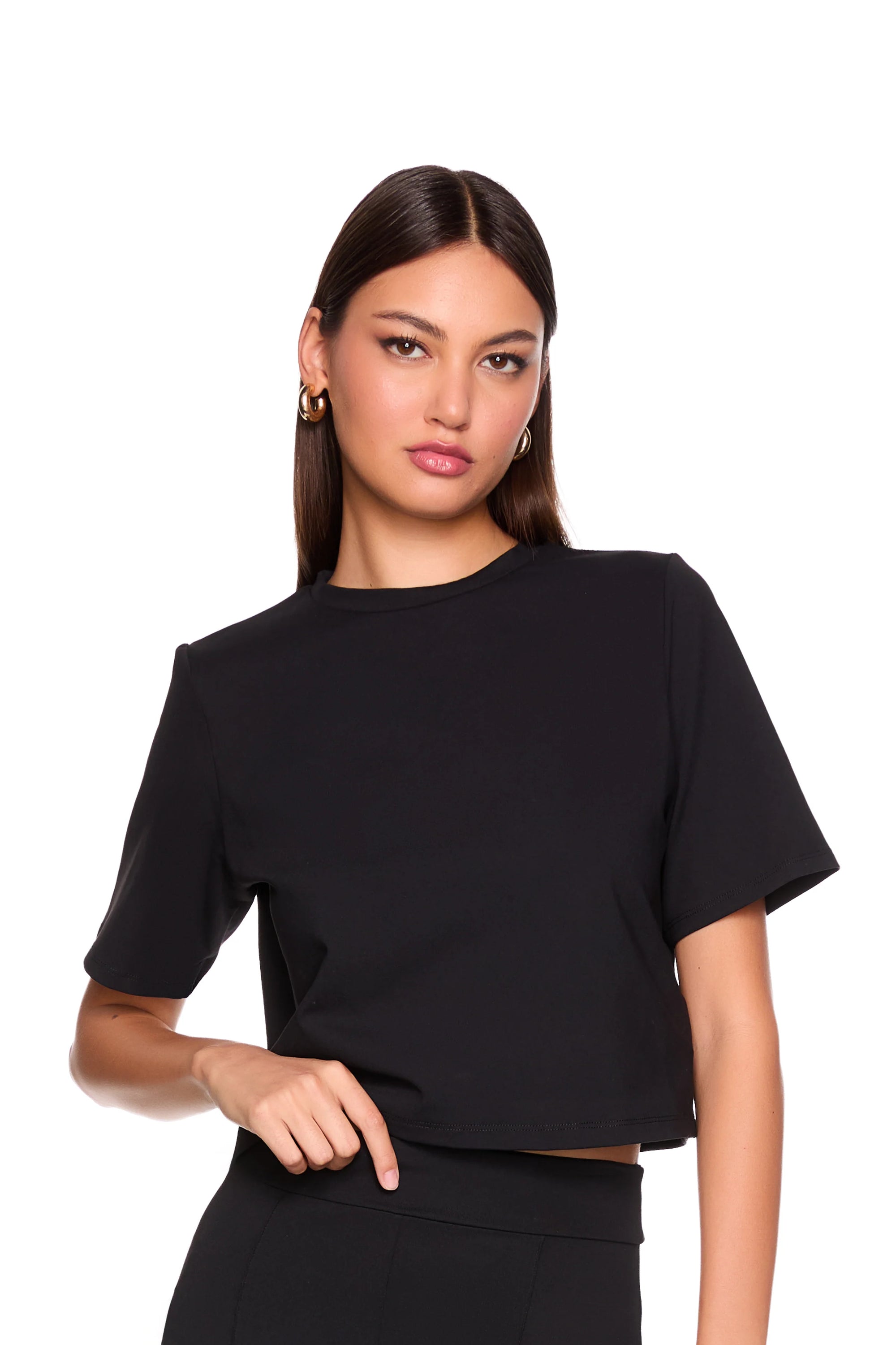 A woman modeling a black short-sleeve crop top with a relaxed, slightly oversized fit, paired with black bottoms, against a solid white background.