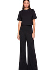 A woman modeling a black short-sleeve crop top and matching black wide-leg pants against a plain white background.