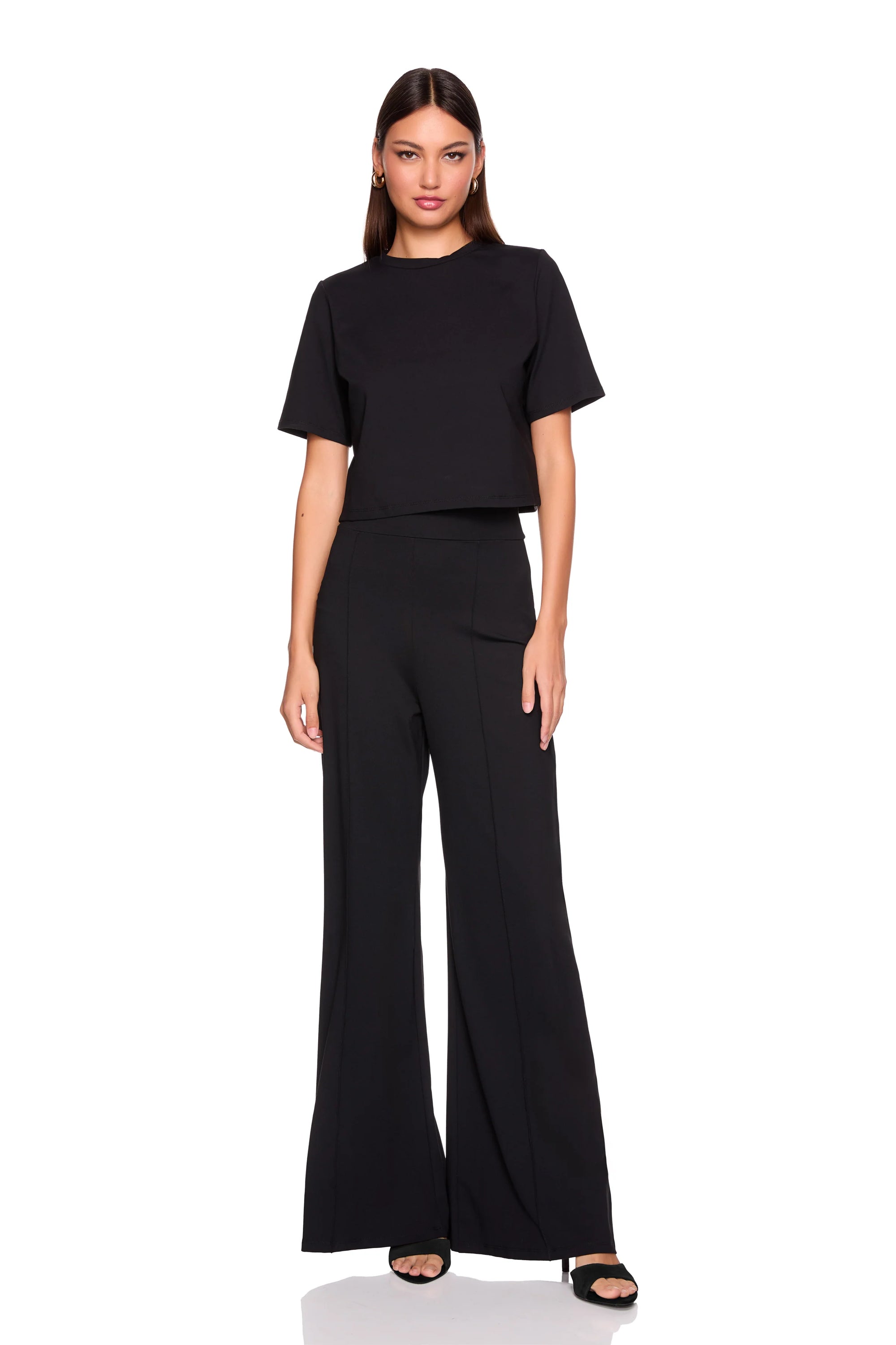 A woman modeling a black short-sleeve crop top and matching black wide-leg pants against a plain white background.