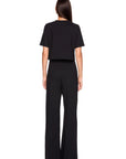 A woman viewed from the back wearing a black short-sleeve cropped top and matching black wide-leg pants against a plain white studio background.