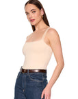 A woman modeling a beige spaghetti-strap camisole top paired with dark blue jeans and a brown belt, photographed against a solid white background.