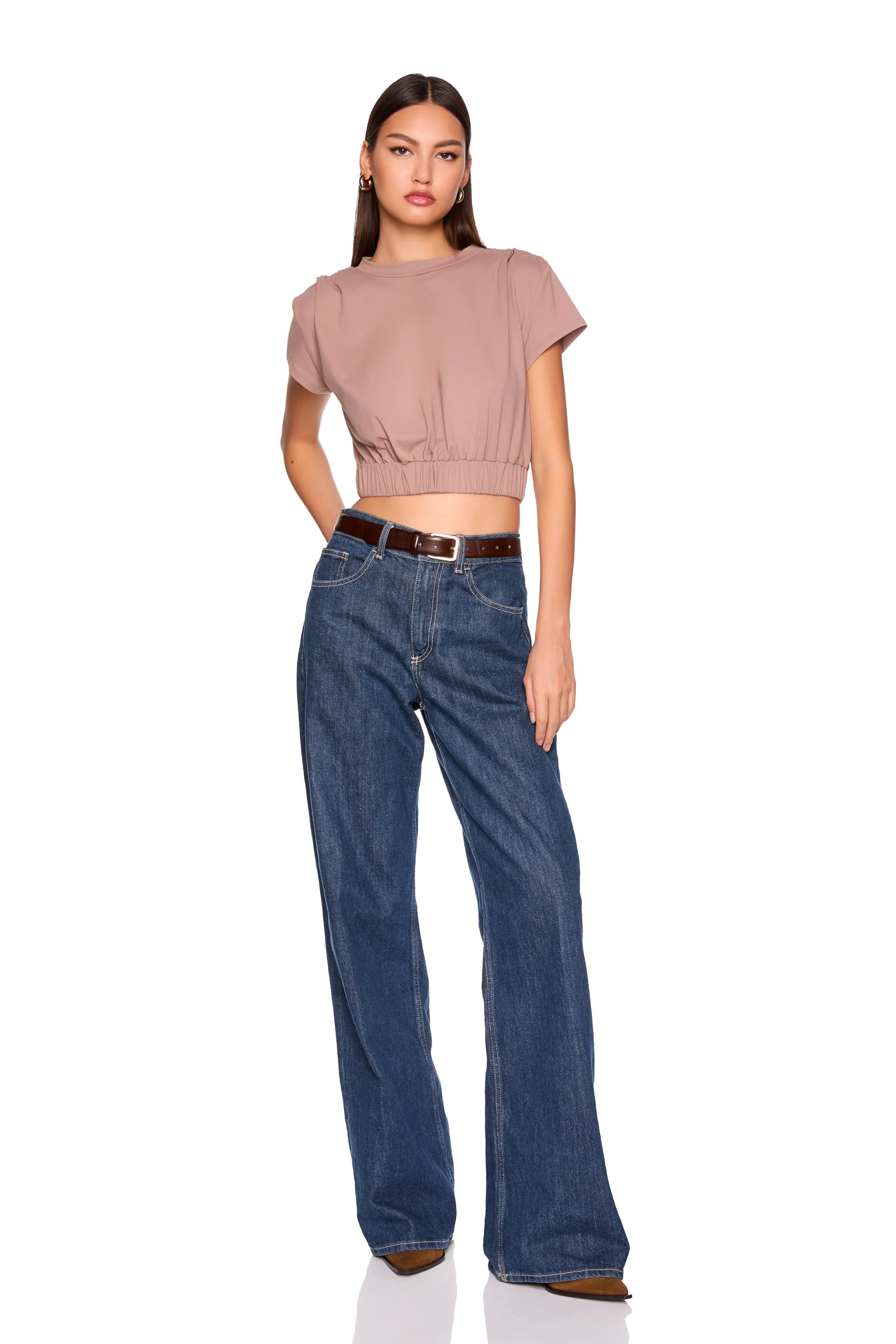 A woman modeling a short-sleeve cropped top in dusty rose and wide-leg blue jeans with a brown belt, shot against a plain white background.