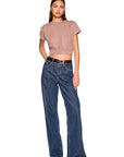 A woman modeling a short-sleeve cropped top in dusty rose and wide-leg blue jeans with a brown belt, shot against a plain white background.