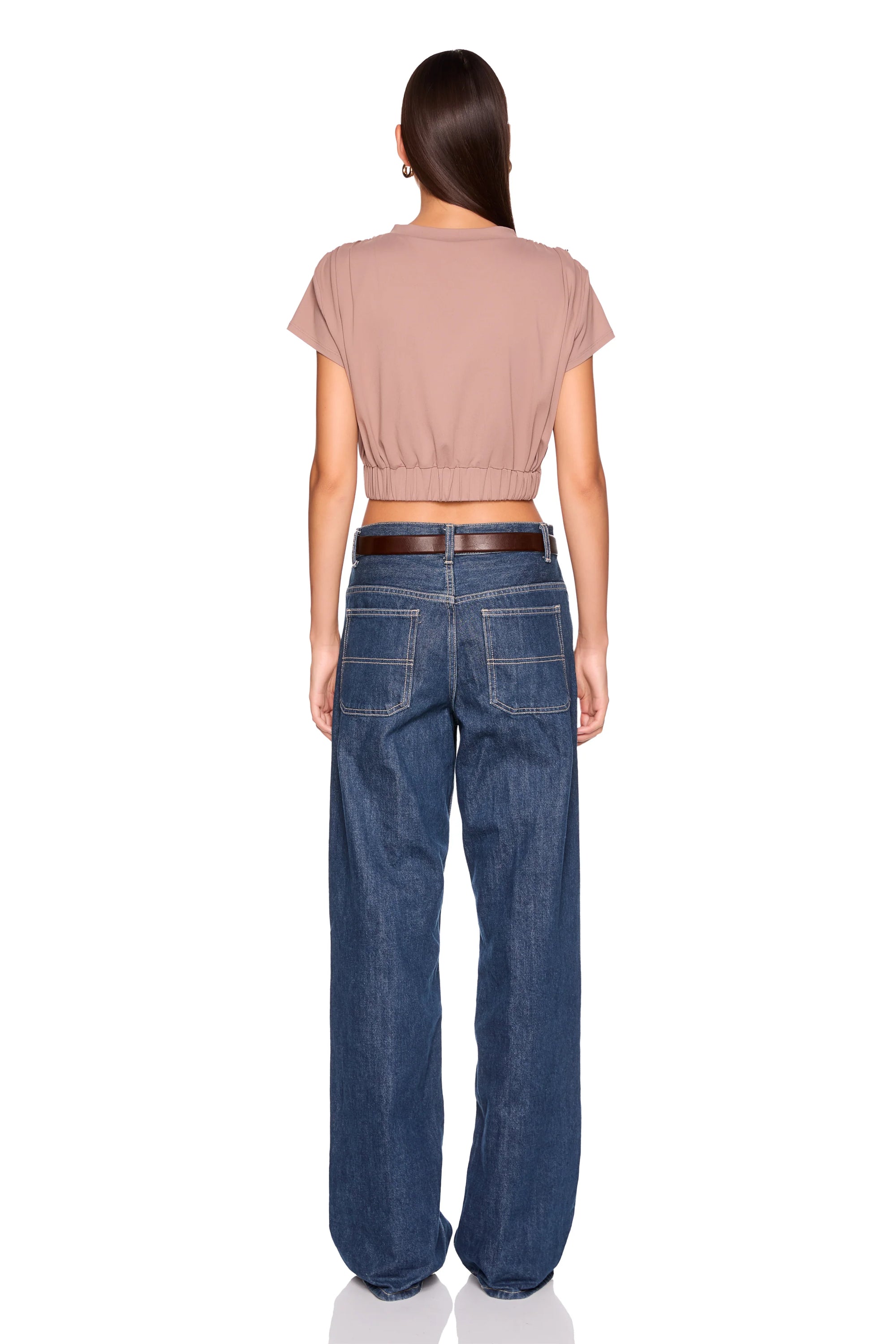 A woman shown from the back wearing a short-sleeve cropped taupe top and wide-leg blue jeans with a dark brown belt, against a plain white background.