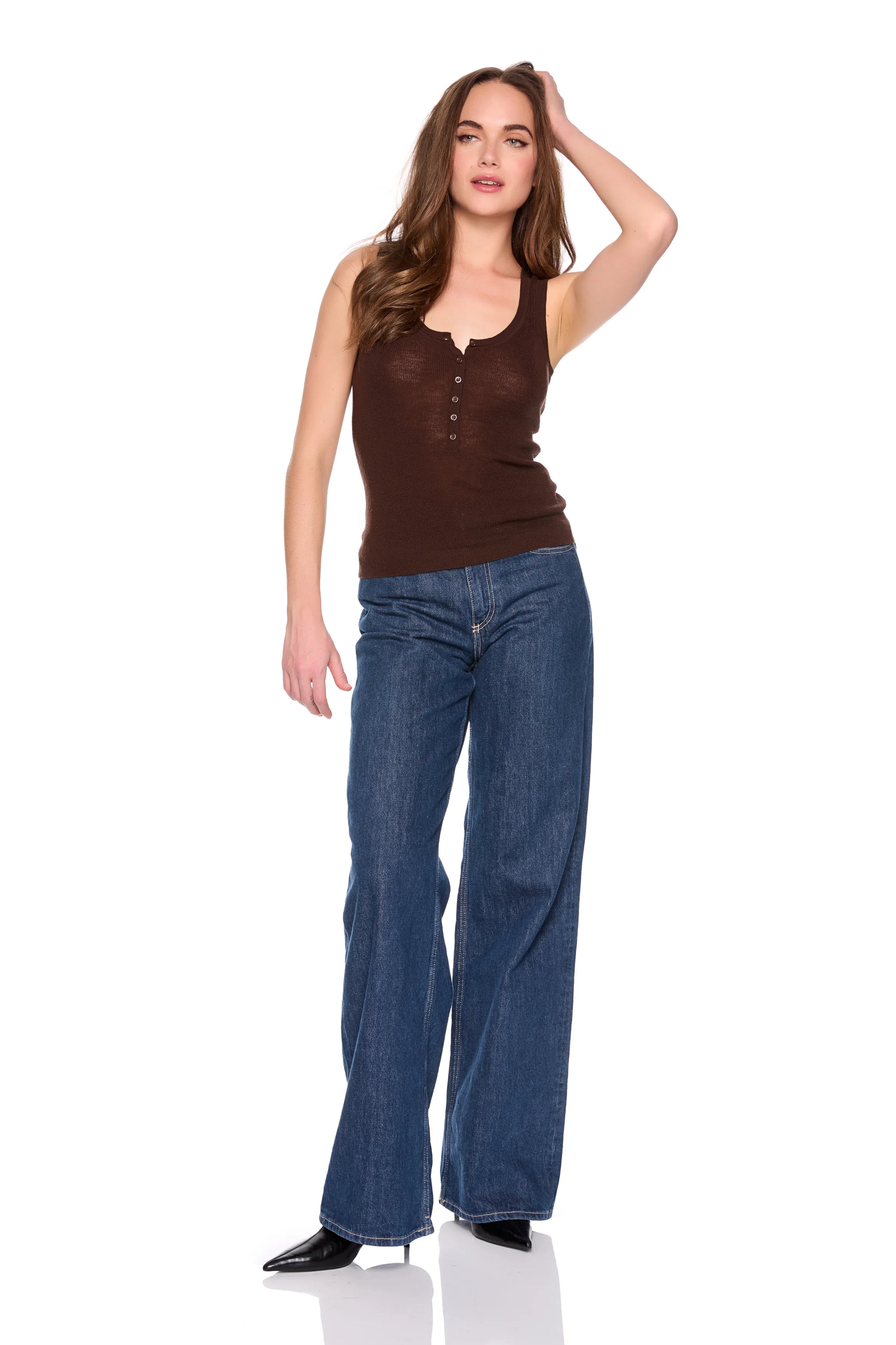 A woman modeling a brown ribbed tank top with a button henley collar and wide-leg blue jeans, standing against a plain white background.