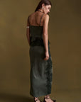 A woman wearing a dark green velvet midi dress with black lace trim, photographed from the back against a solid olive-brown studio background.
