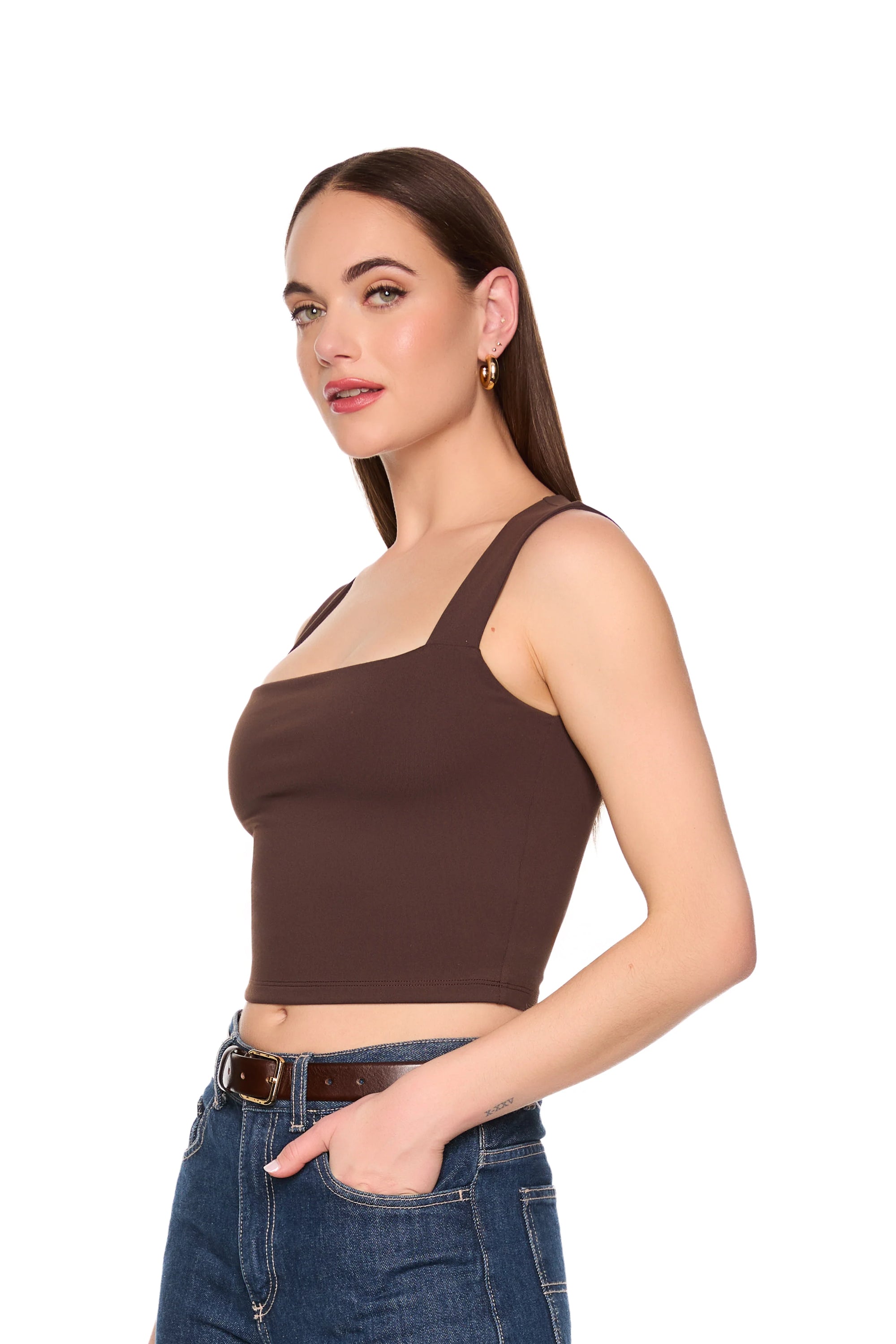 A woman modeling a dark brown square-neck crop top with wide shoulder straps, paired with blue jeans, against a solid white background. Side view