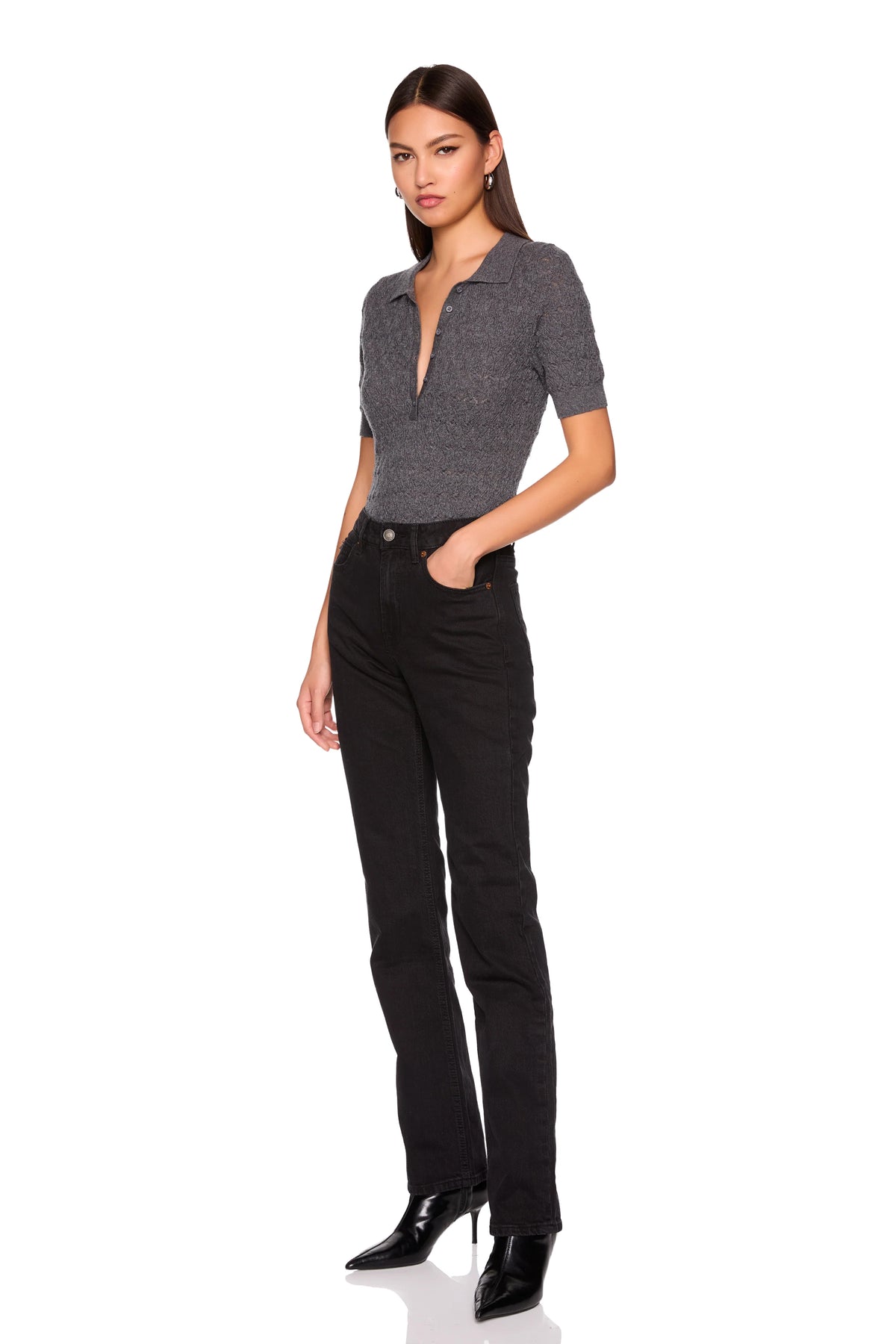 A woman modeling a short-sleeve gray knit polo-style top and black straight-leg jeans with black pointed-toe heels, photographed against a plain white studio background.