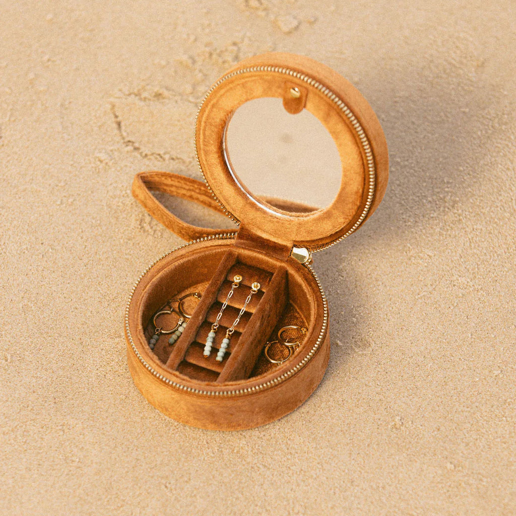Open  jewelry box with small items on a beige sand background