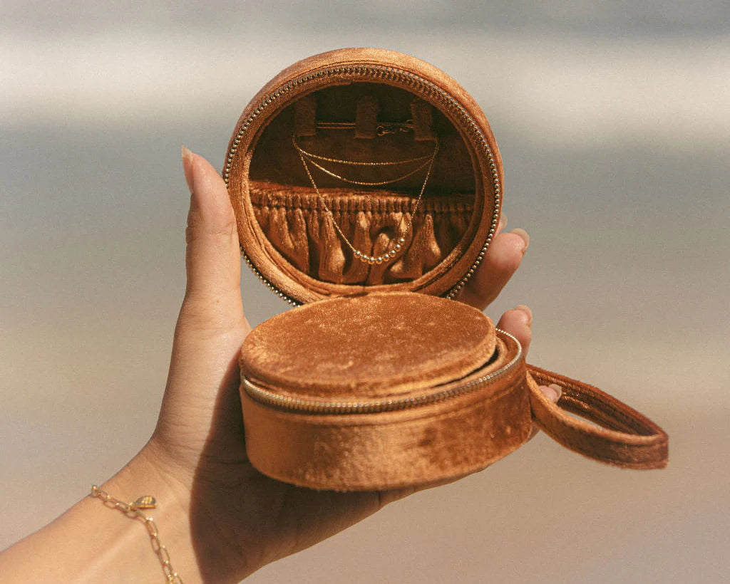 Brown round velvet jewelry box held by a hand with a blurred background