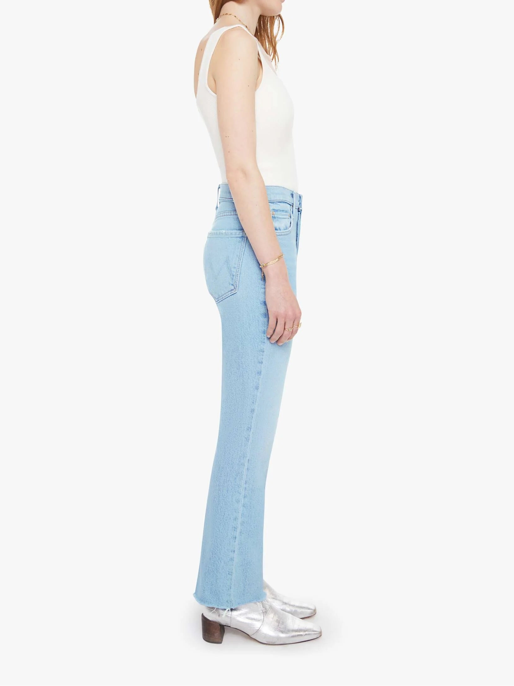 Woman wearing light blue jeans and a white top on a white background side view