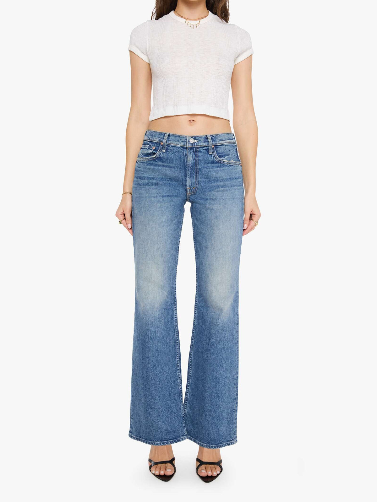 A woman modeling a white short-sleeve cropped top and blue wide-leg jeans against a plain light gray studio background.